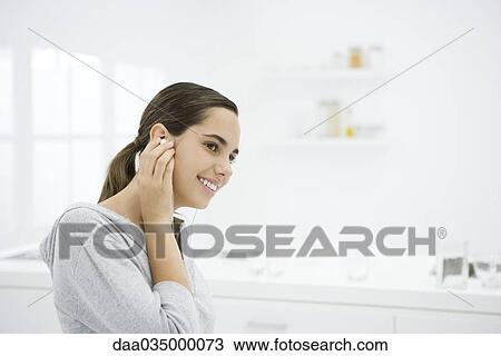 Stock Image - Young female listening to earphones, smiling, looking away. Fotosearch