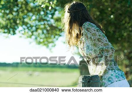 Stock Image - Young hippie woman looking over fence. Fotosearch