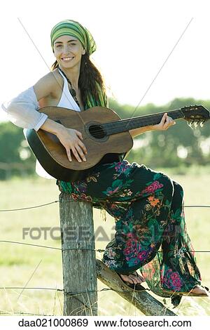 Young hippie woman sitting on fence post, playing guitar View Large Photo Image Stock Photo - Young hippie woman sitting on fence post, playing guitar. Fotosearch