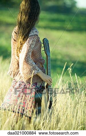 Young hippie woman standing in field, holding guitar, rear view View Large Photo Image Picture - Young hippie woman standing in field, holding guitar, rear view. Fotosearch