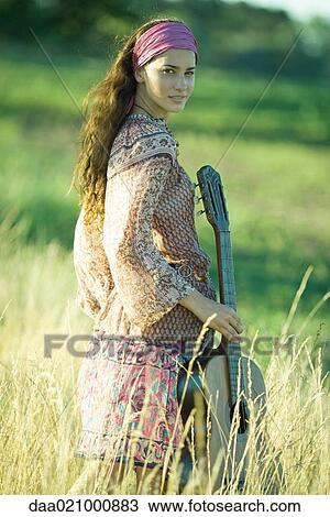 Young hippie woman walking through field, holding guitar View Large Photo Image Stock Image - Young hippie woman walking through field, holding guitar. Fotosearch
