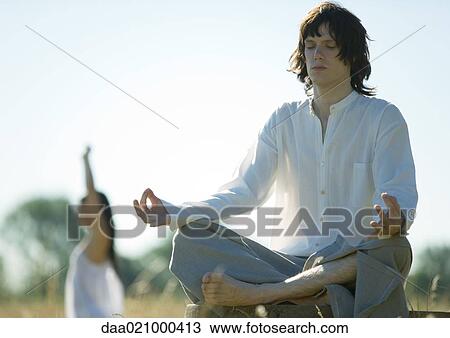 Stock Image - Young male and female doing yoga in field. Fotosearch