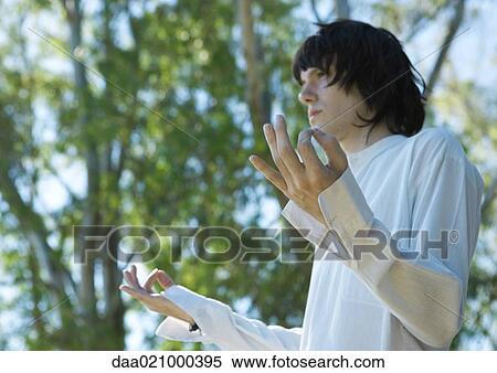 Stock Photography - Young male meditator, low angle view, trees in background. Fotosearch