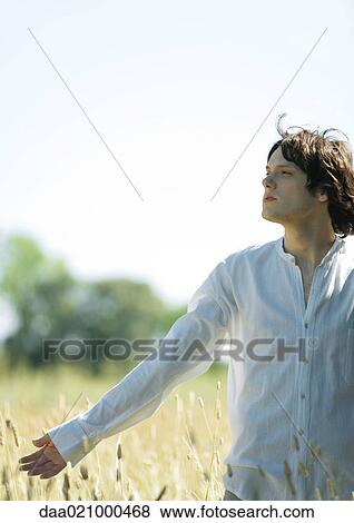 Young male standing in field, arm out, looking away View Large Photo Image Stock Photo - Young male standing in field, arm out, looking away. Fotosearch
