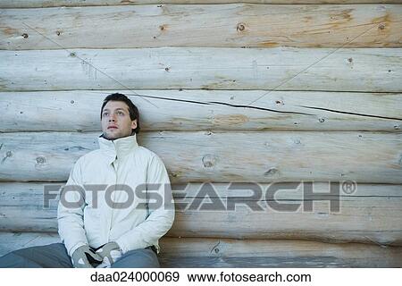 Young man dressed in winter clothing, sitting next to log cabin View Large Photo Image Stock Photo - Young man dressed in winter clothing, sitting next to log cabin. Fotosearch