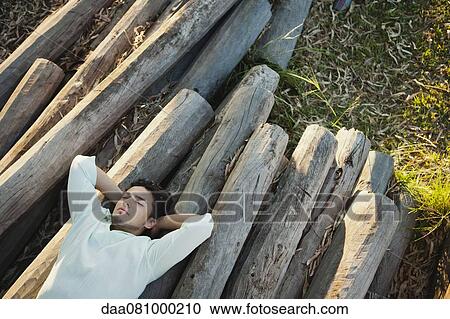 Young man lying on pile of logs, eyes closed View Large Photo Image Stock Image - Young man lying on pile of logs, eyes closed. Fotosearch