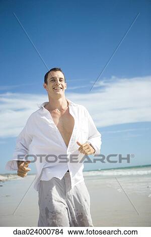 Young man running on beach, smiling View Large Photo Image Picture - Young man running on beach, smiling. Fotosearch