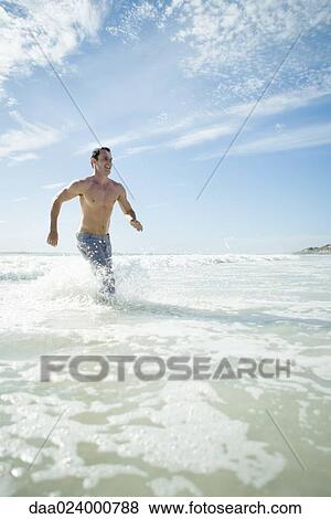 Stock Photo - Young man running through surf on beach. Fotosearch