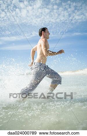 Young man running through surf on beach, full length, side view View Large Photo Image Stock Photo - Young man running through surf on beach, full length, side view. Fotosearch