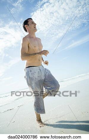 Young man running through surf on beach, low angle view, full length View Large Photo Image Stock Photograph - Young man running through surf on beach, low angle view, full length. Fotosearch