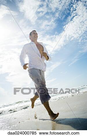 Stock Photography - Young man running through surf on beach, low angle view, full length. Fotosearch