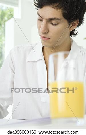Young man sitting and looking down, glass of orange juice in the foreground View Large Photo Image Stock Photo - Young man sitting and looking down, glass of orange juice in the foreground. Fotosearch