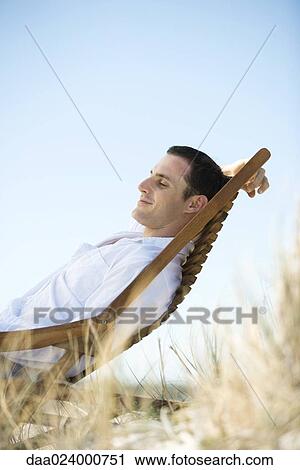 Young man sitting in deck chair View Large Photo Image Stock Image - Young man sitting in deck chair. Fotosearch