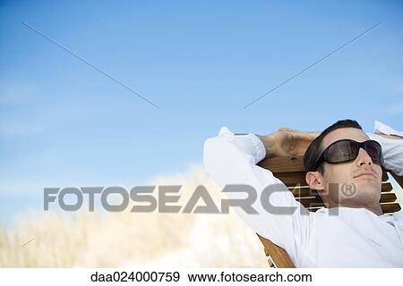 Young man sitting in deck chair, wearing sunglasses View Large Photo Image Stock Photo - Young man sitting in deck chair, wearing sunglasses. Fotosearch
