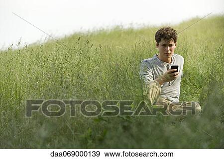 Stock Photo - Young man sitting in grass text messaging. Fotosearch
