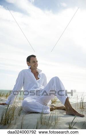 Young man sitting on dune, smiling, full length View Large Photo Image Stock Image - Young man sitting on dune, smiling, full length. Fotosearch