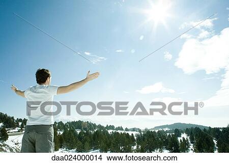 Young man standing, facing snowy mountain landscape with arms up, rear view View Large Photo Image Picture - Young man standing, facing snowy mountain landscape with arms up, rear view. Fotosearch