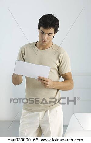 Young man standing, holding document with one hand, writing on it with the other View Large Photo Image Stock Photograph - Young man standing, holding document with one hand, writing on it with the other. Fotosearch