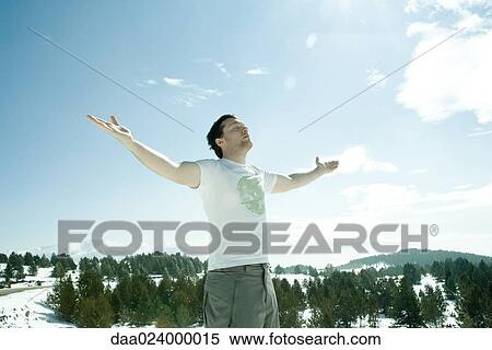 Young man standing in snowy mountain landscape with arms lifted, eyes closed View Large Photo Image Stock Photography - Young man standing in snowy mountain landscape with arms lifted, eyes closed. Fotosearch