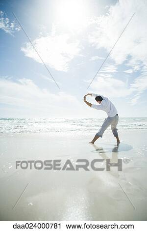 Young man standing in surf, stretching, rear view View Large Photo Image Stock Image - Young man standing in surf, stretching, rear view. Fotosearch
