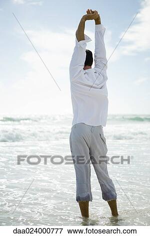 Young man standing in surf, stretching, rear view View Large Photo Image Stock Photo - Young man standing in surf, stretching, rear view. Fotosearch