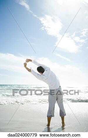 Young man standing in surf, stretching, rear view View Large Photo Image Stock Photo - Young man standing in surf, stretching, rear view. Fotosearch