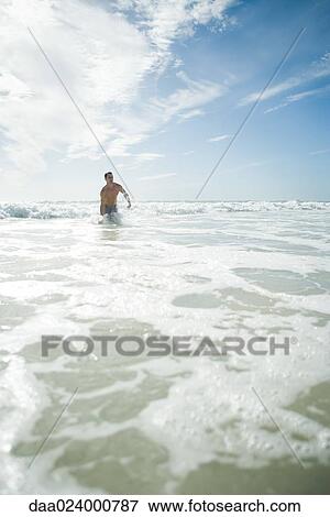 Young man standing waist deep in ocean, in mid-distance View Large Photo Image Stock Photo - Young man standing waist deep in ocean, in mid-distance. Fotosearch