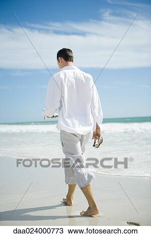 Stock Image - Young man walking on beach, rear view. Fotosearch