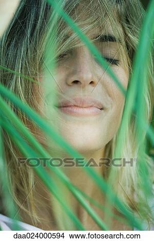 Picture - Young woman among foliage, hair in face, eyes closed, close-up. Fotosearch