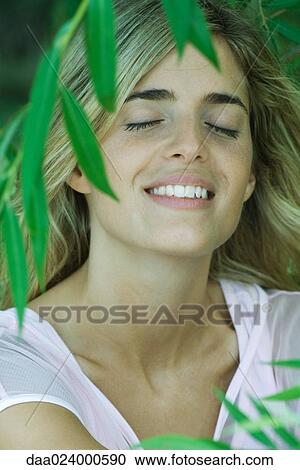 Young woman among foliage, smiling, eyes closed, portrait View Large Photo Image Stock Image - Young woman among foliage, smiling, eyes closed, portrait. Fotosearch