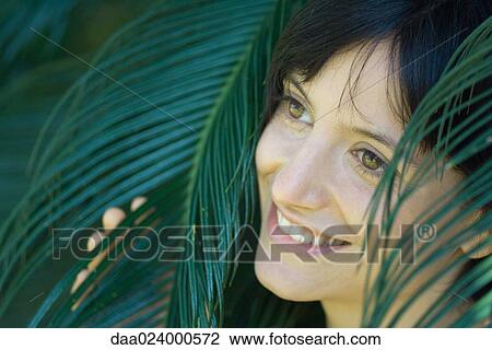 Young woman among palm leaves, smiling, looking away, portrait View Large Photo Image Stock Image - Young woman among palm leaves, smiling, looking away, portrait. Fotosearch