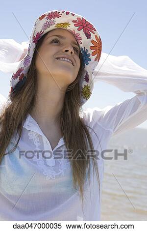 Young woman at beach, holding sunhat on head View Large Photo Image Stock Photography - Young woman at beach, holding sunhat on head. Fotosearch