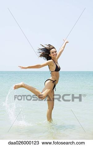 Young woman at the beach jumping, one leg up, arms raised View Large Photo Image Stock Image - Young woman at the beach jumping, one leg up, arms raised. Fotosearch