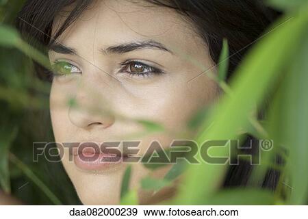Stock Photo - Young woman behind foliage, portrait. Fotosearch