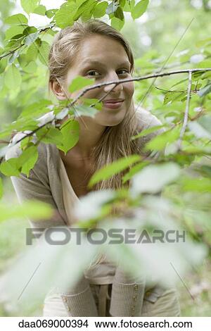 Picture - Young woman behind tree branches. Fotosearch