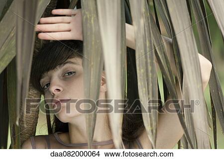 Picture - Young woman behind tropical foliage, portrait. Fotosearch