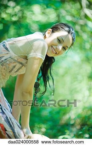 Stock Photo - Young woman bending over outdoors, smiling at camera. Fotosearch