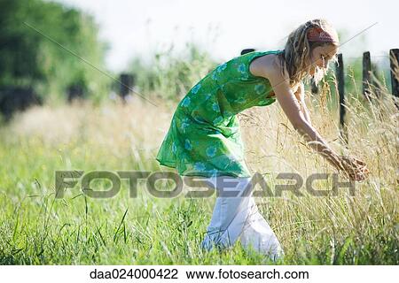 Young woman bending over to touch tall grass in rural field View Large Photo Image Stock Image - Young woman bending over to touch tall grass in rural field. Fotosearch