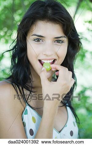 Young woman biting into grape, looking at camera View Large Photo Image Stock Image - Young woman biting into grape, looking at camera. Fotosearch