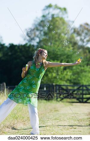 Young woman blowing bubbles in rural field with arm outstretched, standing on one leg View Large Photo Image Stock Photography - Young woman blowing bubbles in rural field with arm outstretched, standing on one leg. Fotosearch