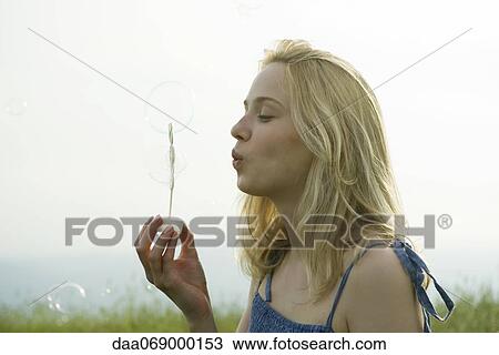 Stock Image - Young woman blowing bubbles with bubble wand. Fotosearch