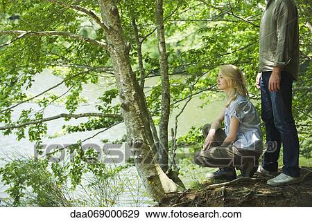 Young woman crouching beside man, looking at lake View Large Photo Image Stock Photo - Young woman crouching beside man, looking at lake. Fotosearch