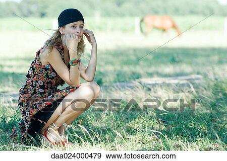 Young woman crouching in field, looking at camera View Large Photo Image Stock Photo - Young woman crouching in field, looking at camera. Fotosearch