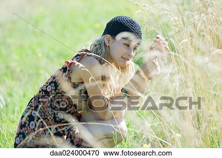 Young woman crouching in field, touching tall grass View Large Photo Image Stock Image - Young woman crouching in field, touching tall grass. Fotosearch