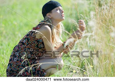 Young woman crouching in field, touching tall grass and looking up View Large Photo Image Stock Image - Young woman crouching in field, touching tall grass and looking up. Fotosearch