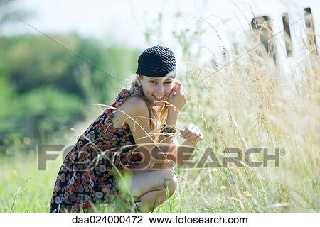 Young woman crouching in field, touching tall grass and smiling at camera View Large Photo Image Stock Image - Young woman crouching in field, touching tall grass and smiling at camera. Fotosearch