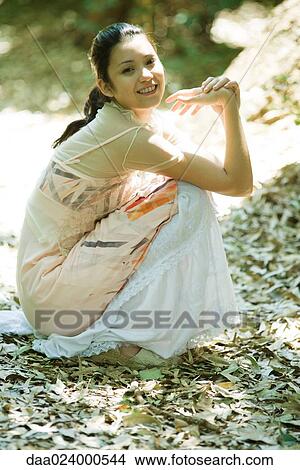 Picture - Young woman crouching in leaves, smiling at camera. Fotosearch