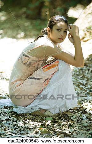 Young woman crouching in leaves, looking at camera View Large Photo Image Stock Image - Young woman crouching in leaves, looking at camera. Fotosearch