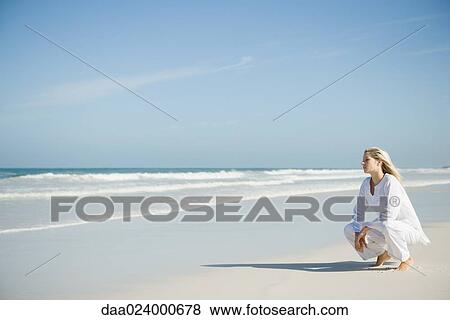Stock Photo - Young woman crouching on beach. Fotosearch