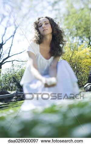 Young woman crouching outdoors, eyes closed, viewed from surface level View Large Photo Image Stock Photo - Young woman crouching outdoors, eyes closed, viewed from surface level. Fotosearch